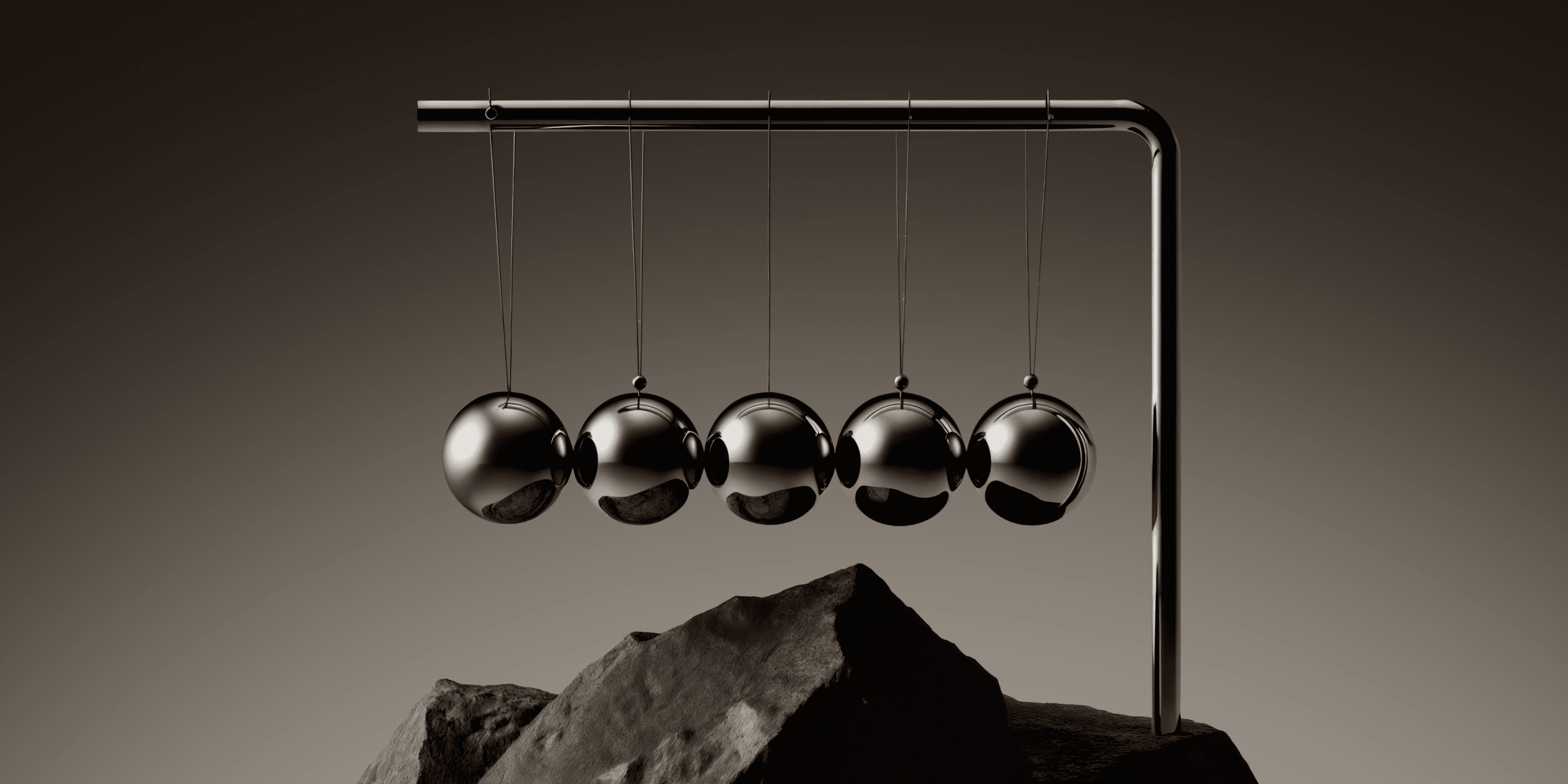 Newton's cradle with five polished chrome balls hanging from a metal frame, resting on a jagged rock against a dark brown background