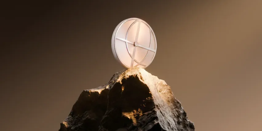 A white spherical object with a cross-shaped metal frame balanced on the tip of a rocky peak, against a warm brown gradient background.