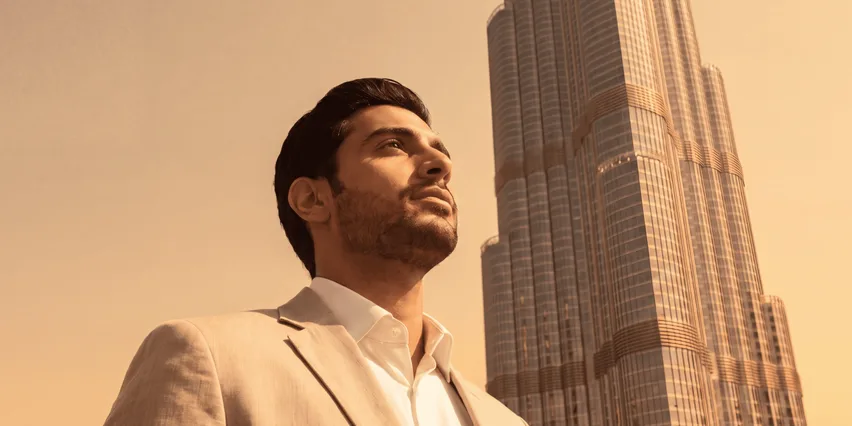 Man in a light beige suit and white shirt looking upward, standing before the Burj Khalifa at golden hour, Dubai.