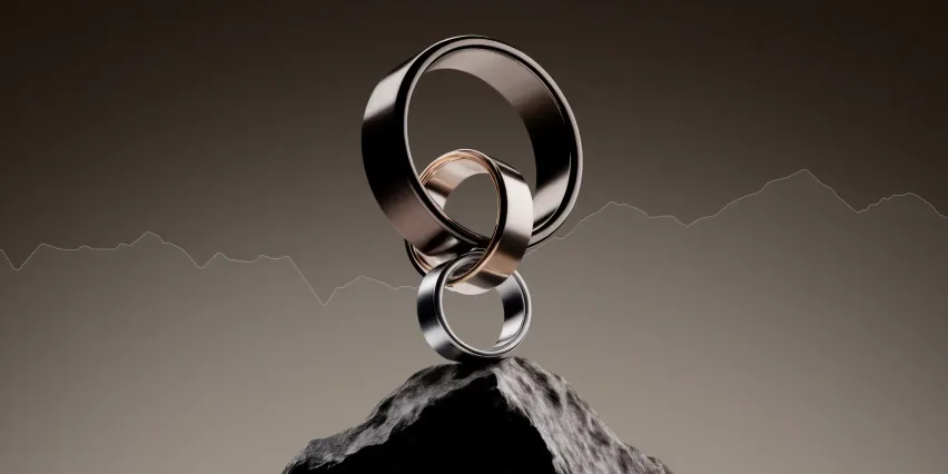Three interlocking metal rings balanced on a rocky peak, with a faint line chart running across the background