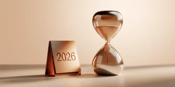 Brushed copper desk calendar engraved 2026 beside a glass hourglass with sand running through