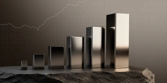 Row of polished metal blocks rising in height like a bar chart, standing on dark rock in front of an upward-trending line graph