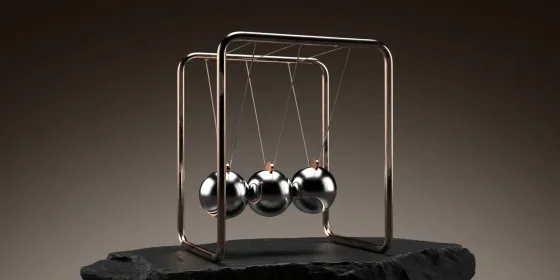 Chrome Newton's cradle with three polished steel balls hanging from a copper frame on a black slate slab, dark background.