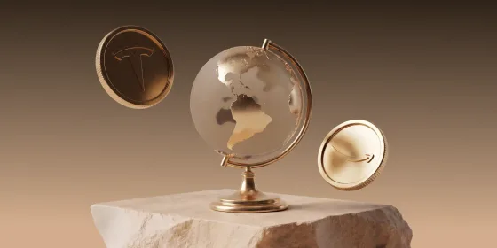 Gold coins stamped with the Tesla and Amazon logos beside a glass globe on a stone plinth, representing fractional share investing from the UAE
