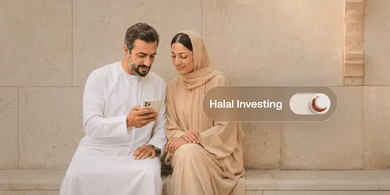 A couple in traditional Emirati dress sit against a sandstone wall reviewing an investment app on a smartphone, next to a toggle switch labelled "Halal Investing" with a crescent moon icon.